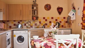 A compact kitchen with a washing machine, a dining table set for two, and a small refrigerator. - 2 bedroom accommodation in Portree (Portree)