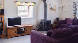 A cozy living room with a television, wooden entertainment unit, purple sofa, and a wood-burning stove. - 3 bedroom accommodation in Westerdale, near Castleton (Westerdale, near Castleton)