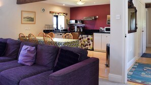 A living room with a purple sofa, a dining area with a table and chairs, and a kitchen with basic appliances. - 3 bedroom accommodation in Westerdale, near Castleton (Westerdale, near Castleton)