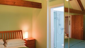 A bedroom with a wooden headboard, a bedside table with a lamp, a green bedspread, and a glass shower enclosure. - 3 bedroom accommodation in Westerdale, near Castleton (Westerdale, near Castleton)