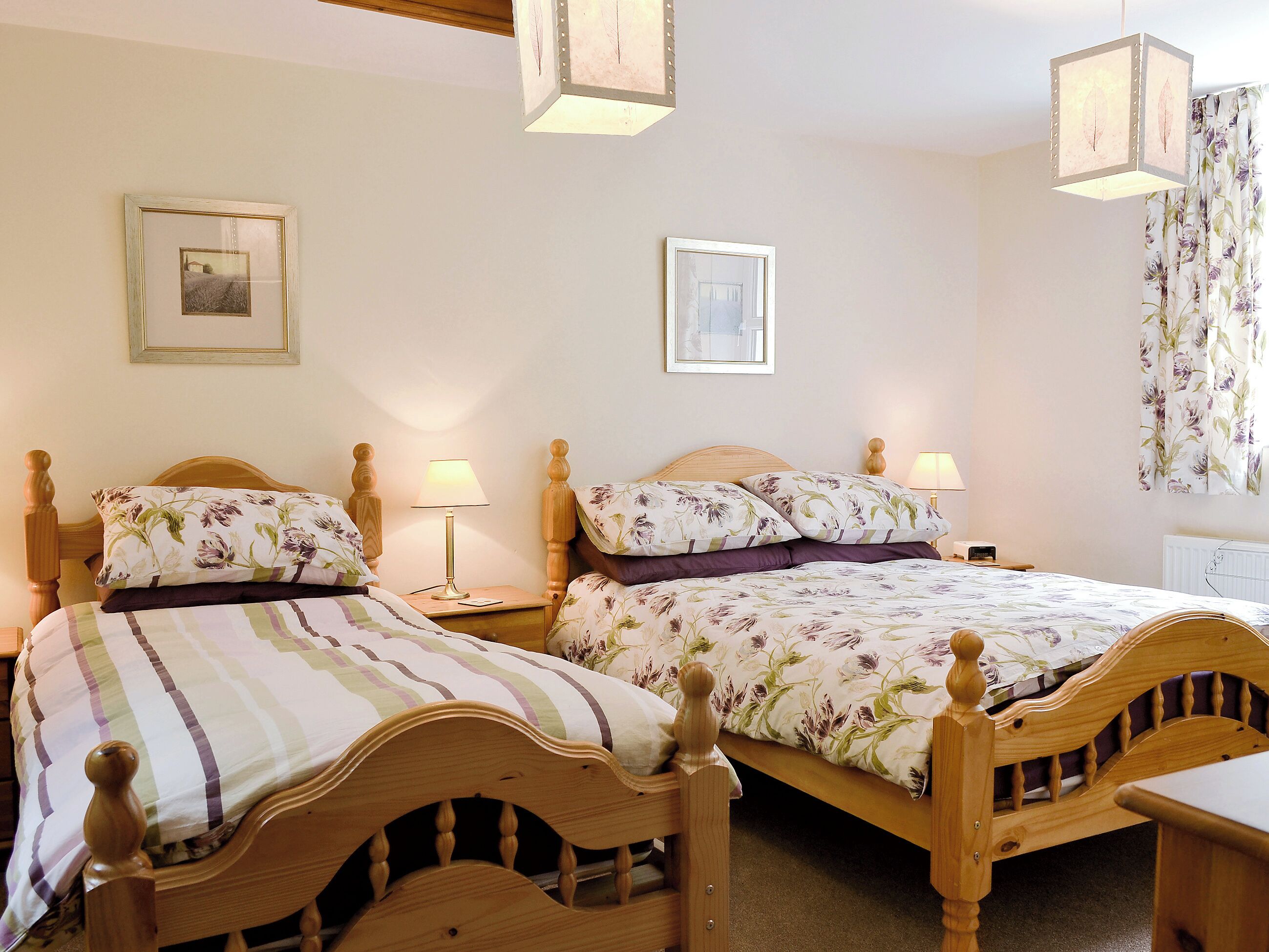 A bedroom with two wooden beds, each with floral bedding and bedside lamps.