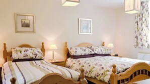 A bedroom with two wooden beds, each with floral bedding and bedside lamps.