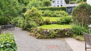 A garden with a stone wall, a small bridge, and a house in the background.