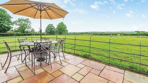 A patio with a table and chairs, an umbrella, and a view of a green field. - 3 bedroom accommodation in Arkleby, near Cockermouth (Arkleby, near Cockermouth)