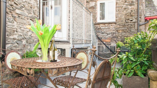 A rustic outdoor seating area with a stone wall, a metal table, and chairs. - 3 bedroom accommodation in Windermere (Windermere)