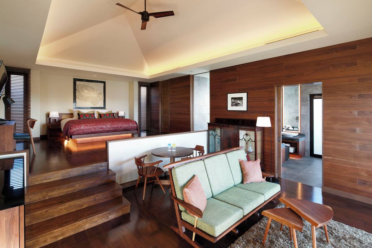 Een moderne hotelkamer met een houten vloer, een bank, een bed, een zithoek en een trap.