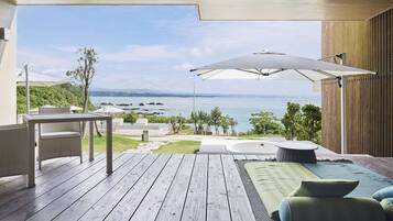 Eine Holzterrasse mit Tisch und Stühlen, einem großen Sonnenschirm und Blick aufs Meer.