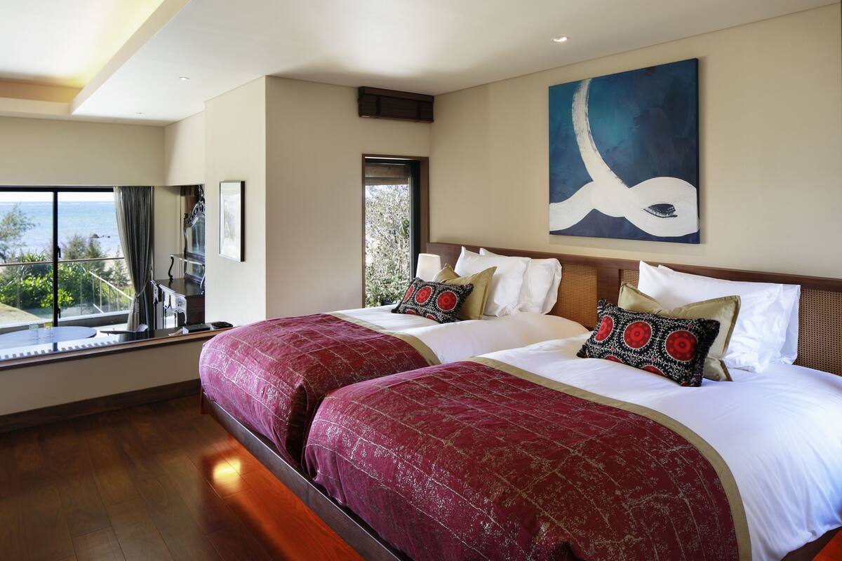 Een hotelkamer met twee bedden, grote ramen en uitzicht op zee.
