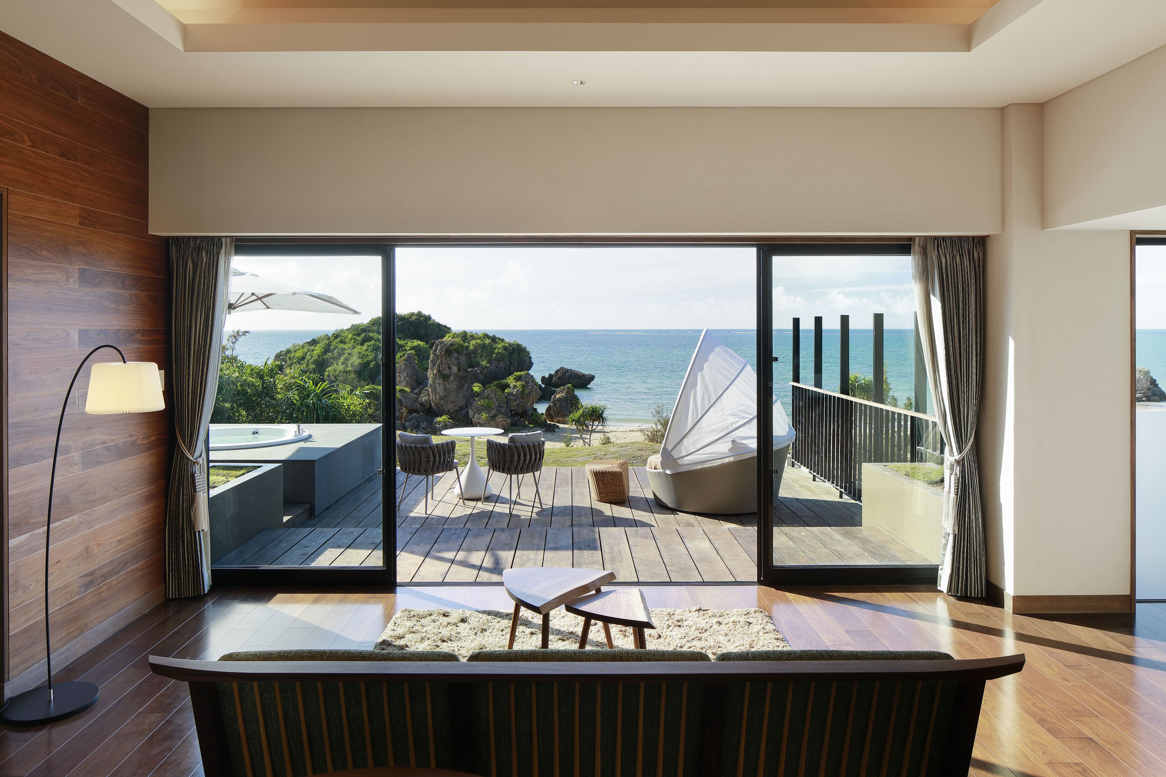 Ein modernes Zimmer mit einer großen Schiebeglastür, die auf eine Terrasse mit Gartenmöbeln und Meerblick führt.