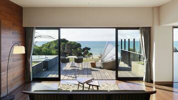 Ein modernes Zimmer mit einer großen Schiebeglastür, die auf eine Terrasse mit Gartenmöbeln und Meerblick führt.