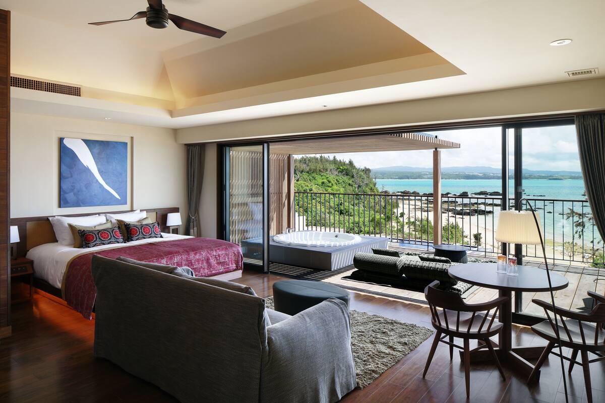 Een moderne hotelkamer met een groot bed, een slaapbank, een zithoek en een balkon met uitzicht op zee.