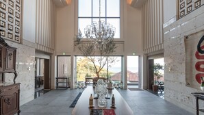 A spacious lobby with a large chandelier, a central table with bottles, and a view of the outdoors through large windows. - The Hiramatsu Hotels & Resorts Ginoza (Ginoza)