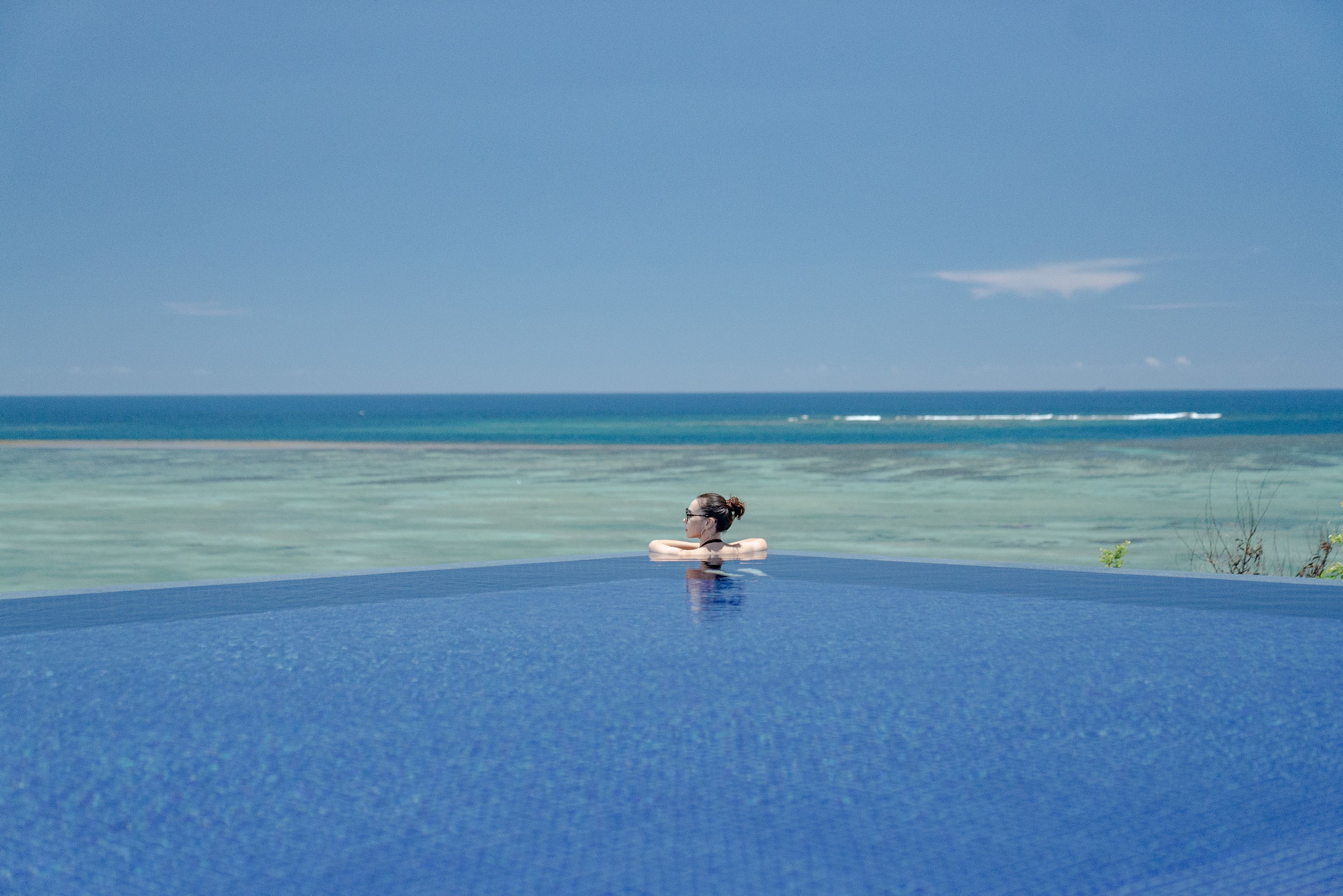 Una persona descansando en una piscina azul infinita con vistas al océano.