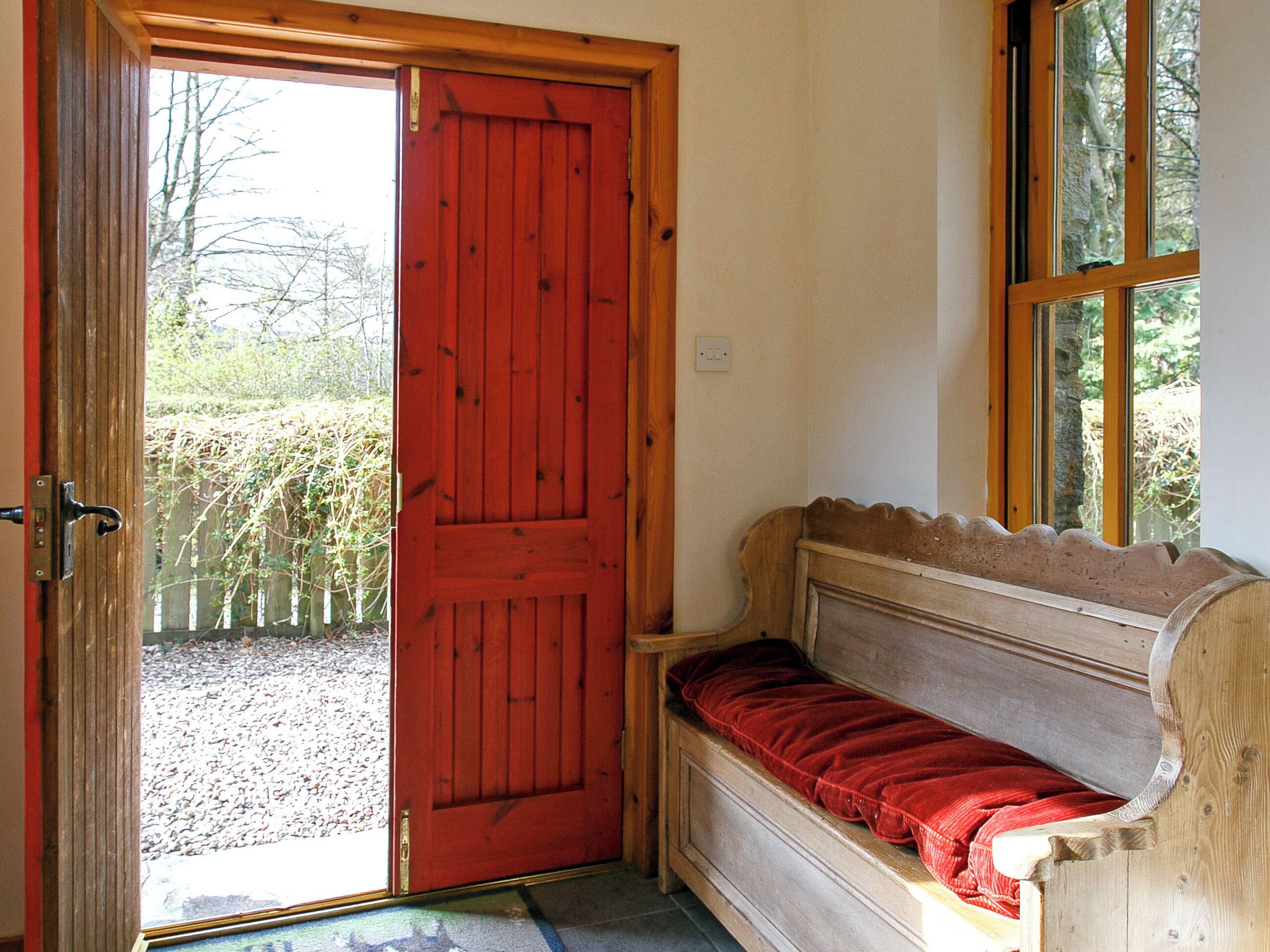 Una habitación con una puerta roja, un banco con cojín rojo y una ventana con vista a árboles.