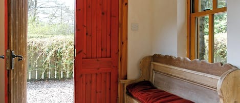 Una habitación con una puerta roja, un banco con cojín rojo y una ventana con vista a árboles.