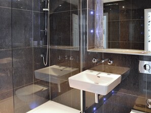 Une salle de bain moderne avec une douche à parois de verre, un lavabo blanc et un miroir au-dessus du lavabo.