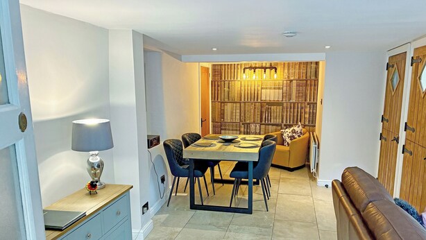 A dining area with a table, chairs, a lamp, a bookshelf, and a sofa. - A traditional Lakeland cottage situated in the heart of Portinscale village. (Portinscale, near Keswick)