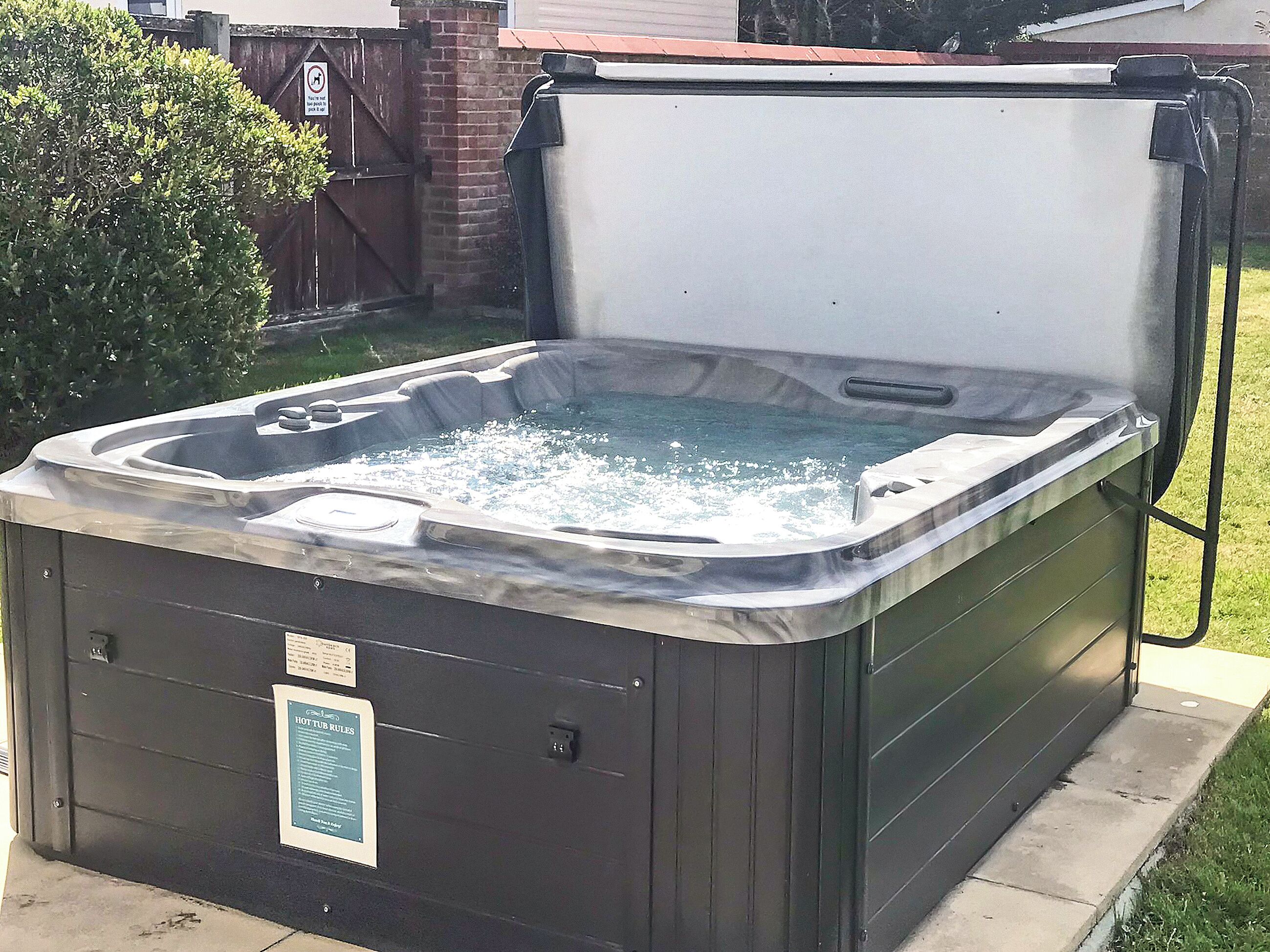A hot tub with a cover, a control panel, and a sign with hot tub rules.