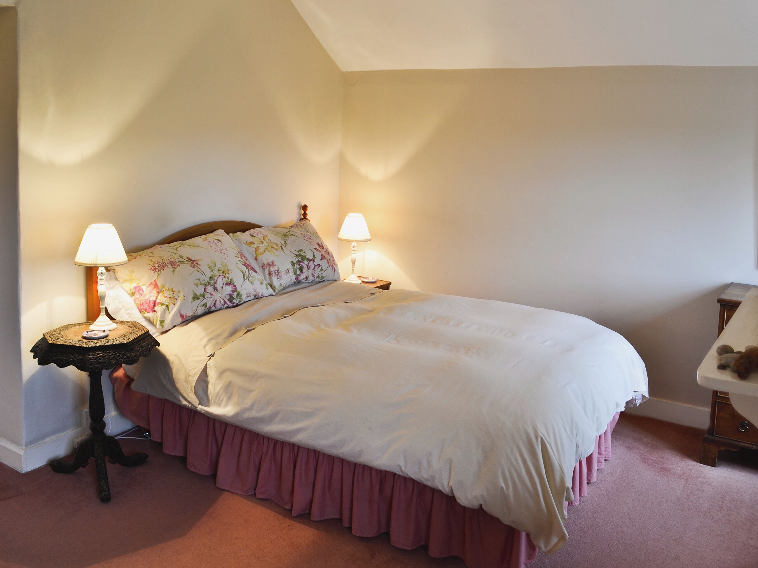 Un lit bien fait, agrémenté d’un coussin à motifs floraux, de deux lampes de chevet et d’une petite table avec une lampe.