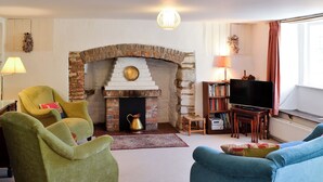 Ein Wohnzimmer mit Kamin aus Backstein, grünen und blauen Sesseln, einem Fernseher und einem Bücherregal.