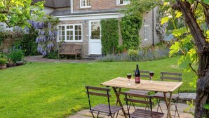 Ein Ziegelhaus mit Garten, einer hölzernen Bank und einem Tisch mit Weingläsern und einer Weinflasche.
