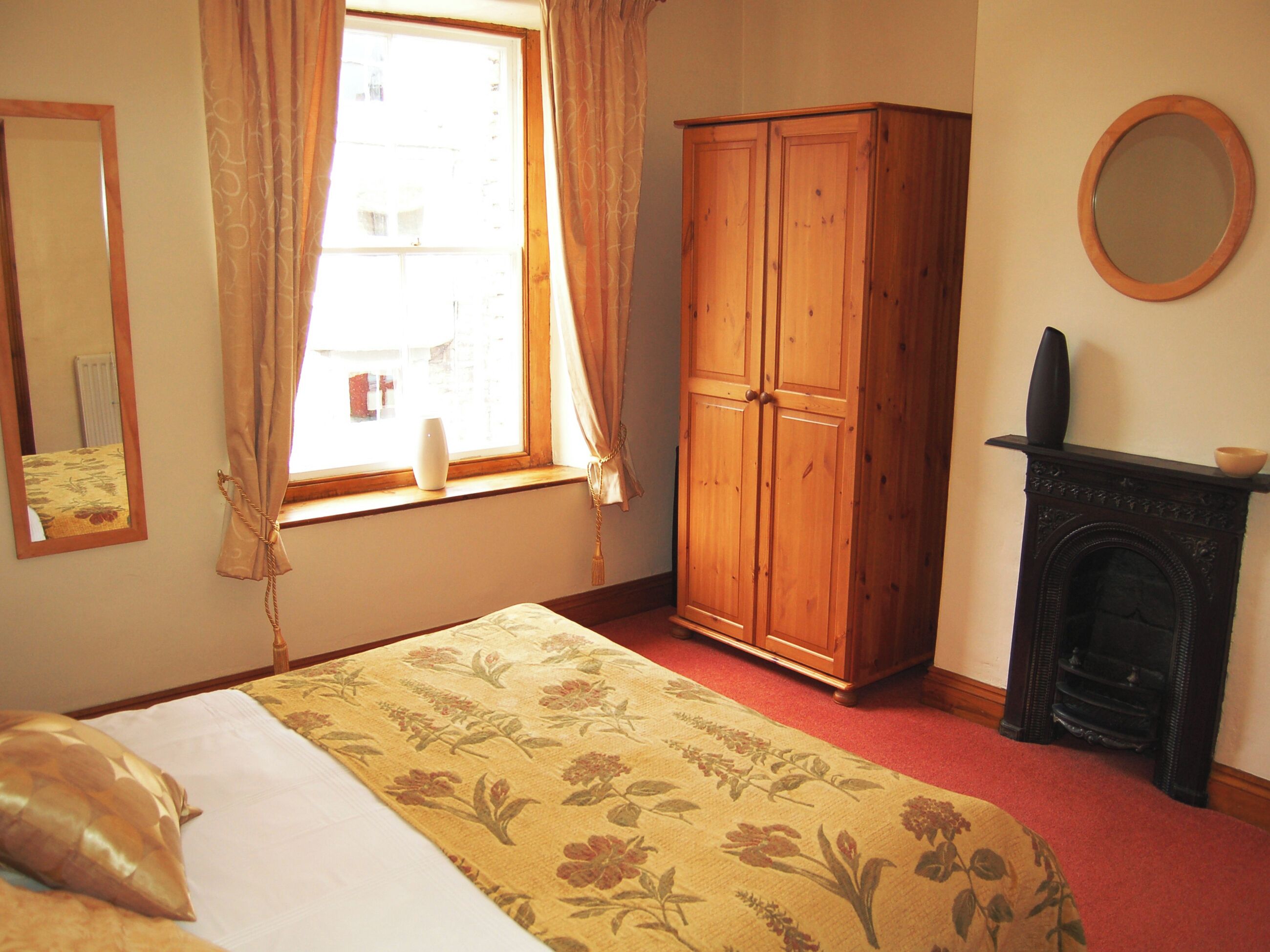 A bedroom with a bed, a wardrobe, a fireplace, and a window with curtains.
