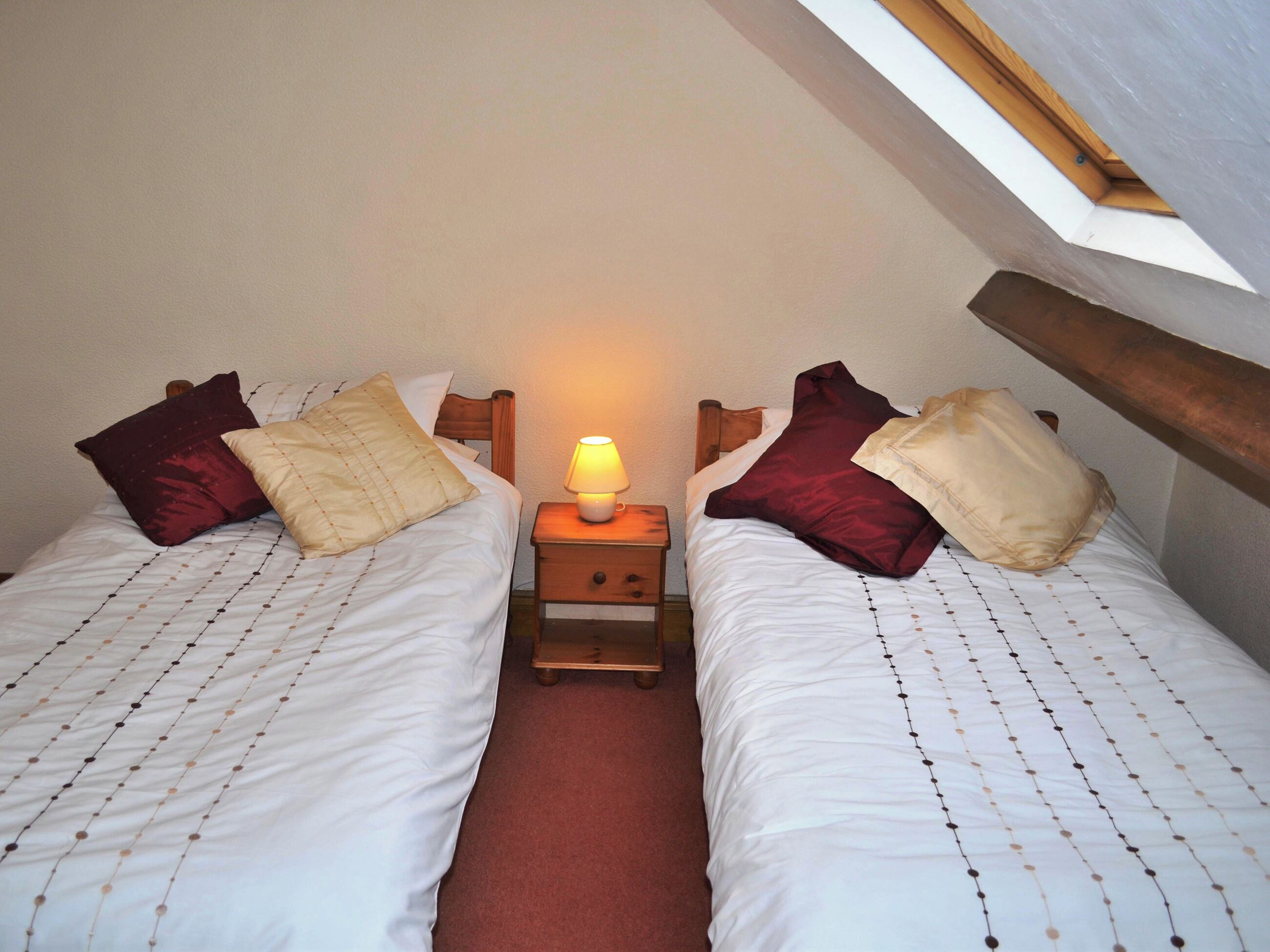 Een kleine, gezellige kamer met twee eenpersoonsbedden, een nachtkastje met een lamp en een schuine plafond met een dakraam.