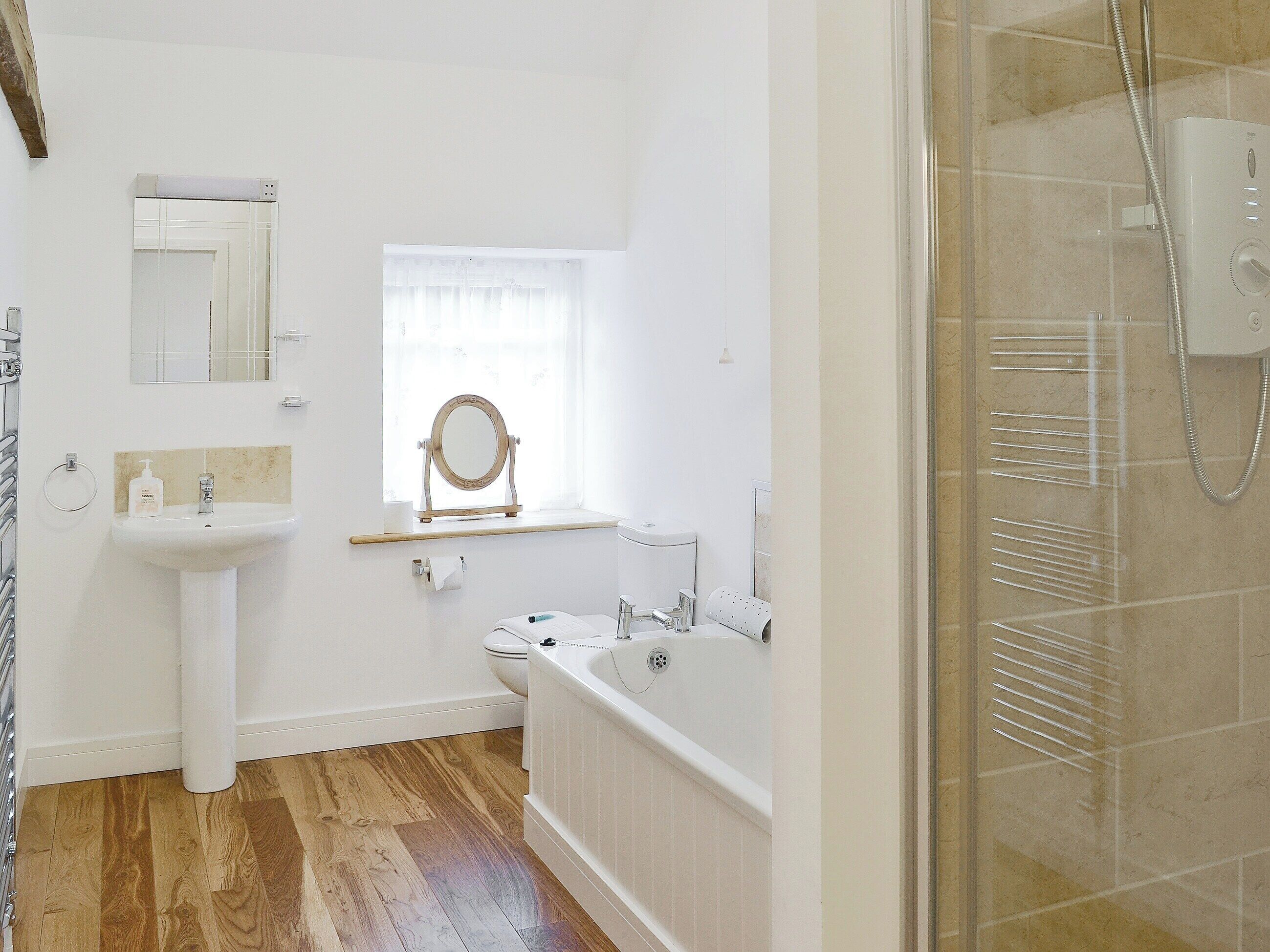 A bathroom with a sink, vanity, mirror, window, toilet, bathtub, and shower.