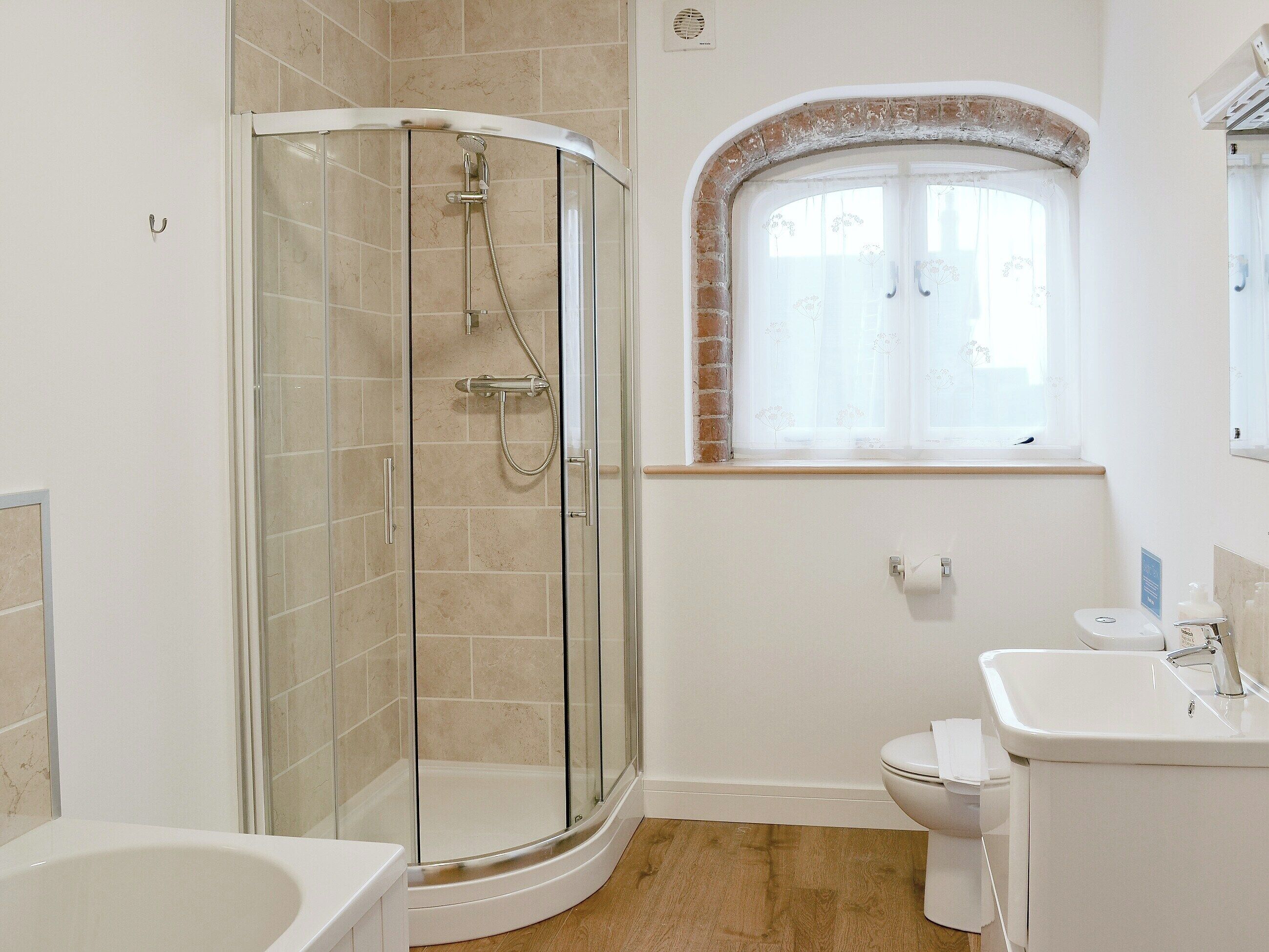 A bathroom with a glass-enclosed shower, a toilet, a sink, and a window with a decorative arch.