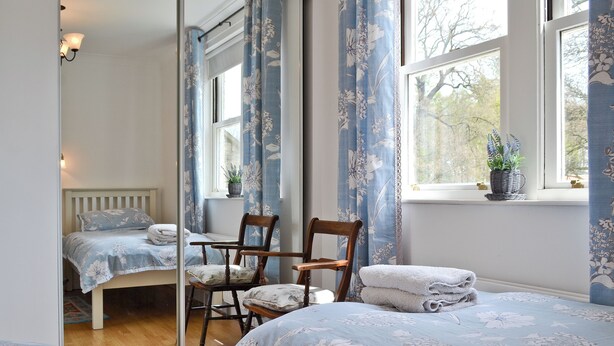 A bedroom with a bed, a chair, a mirror, and a window with curtains. - 2 bedroom accommodation in Staindrop, near Barnard Castle (Staindrop, near Barnard Castle)