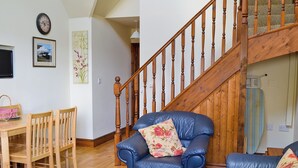 Un salon avec un canapé en cuir bleu, une table à manger en bois, des chaises, un escalier et une horloge murale.