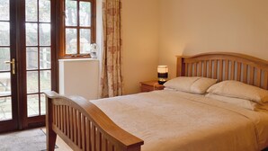Une chambre à coucher avec un lit en bois, une table de chevet avec une lampe, une fenêtre avec des rideaux et une porte donnant sur l’extérieur.