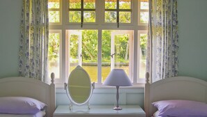 A bedroom with two beds, a dresser, a mirror, a lamp, and a window with a view of greenery. - 3 bedroom accommodation in Hoveton, near Wroxham, Norwich (Hoveton, near Wroxham, Norwich)