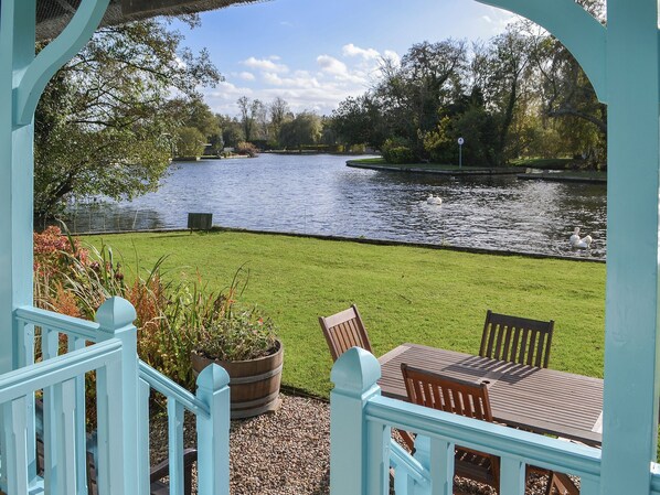 A view of a river with ducks, a grassy area, and a wooden table with chairs.
