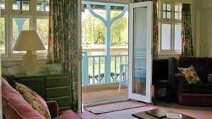 A room with a sofa, a table with a lamp, a chair, and a view through a door to an outdoor area with a railing. - 3 bedroom accommodation in Hoveton, near Wroxham, Norwich (Hoveton, near Wroxham, Norwich)