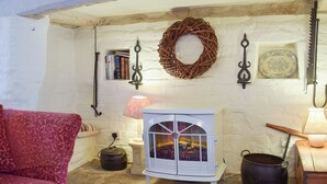 Ein gemütlicher Raum mit einem rot gemusterten Sofa, einem weißen Schrank mit Glastüren, einem Korbschild an der Wand und einem rustikalen Herd.
