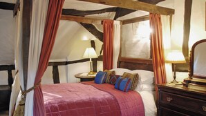 Ein traditionell eingerichtetes Zimmer mit einem Himmelbett, einem Holzschrank und einem Nachttisch mit Lampe.