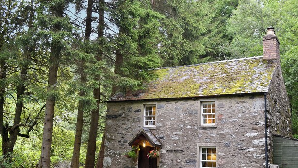 A stone cottage with a wooden door, a bench, and a small table outside.