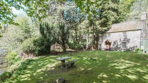A stone building with a grassy yard, a picnic table, and a small pond.