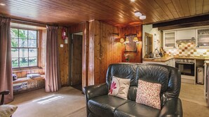 A cozy living room with a leather sofa, a wooden ceiling, and a view into the kitchen.