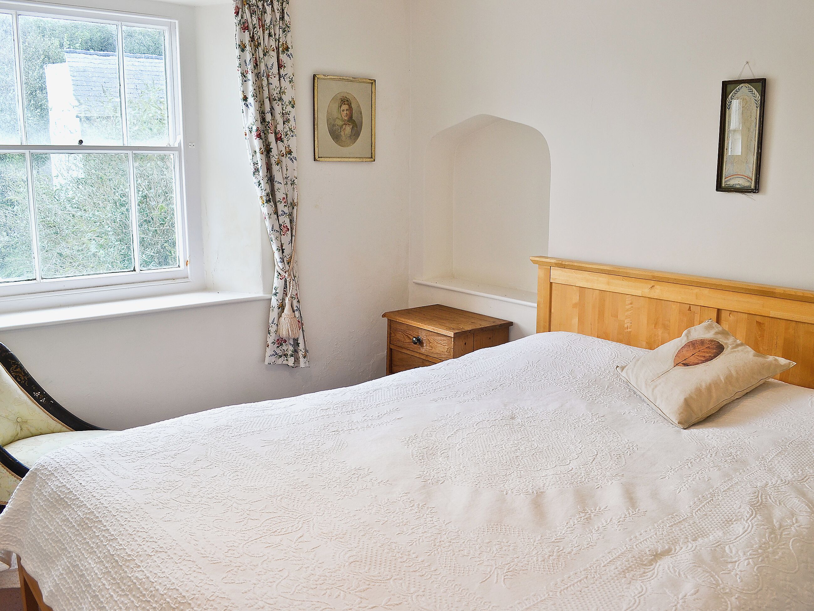 A bedroom with a large bed, a wooden nightstand, a small table, and a window with curtains.