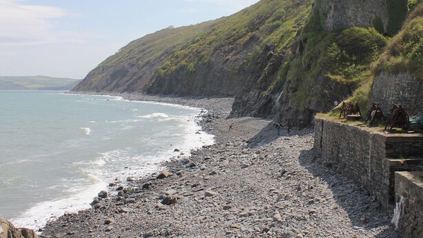 Een rotsachtig strand met een stenen muur en een huis op een heuvel.