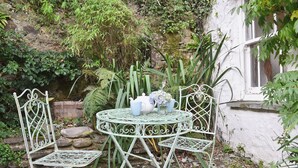 Een ronde metalen tafel met stoelen, een plant in pot en een raam met uitzicht op groen.