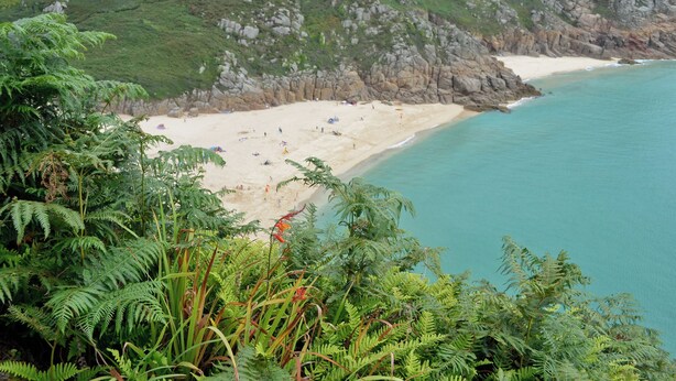 A coastal beach with rocky cliffs and dense greenery.