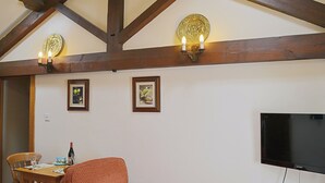 A room with a wooden ceiling, a dining table with chairs, a sofa, and a flat-screen TV mounted on the wall.