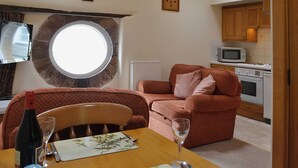 A dining area with a table set for two, a red sofa, a microwave, and a stove in the background.