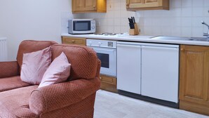 A compact kitchen with wooden cabinets, a microwave, a stove, and a dishwasher.