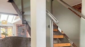 Un escalier moderne avec des rampes en métal et des marches en bois, menant à une pièce dotée d’une grande fenêtre et d’une décoration murale.