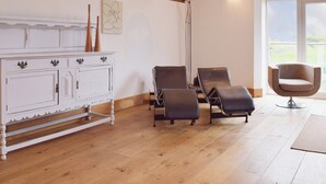 Une pièce avec un meuble blanc, deux fauteuils en cuir, un fauteuil moderne et une grande fenêtre donnant sur un beau paysage.