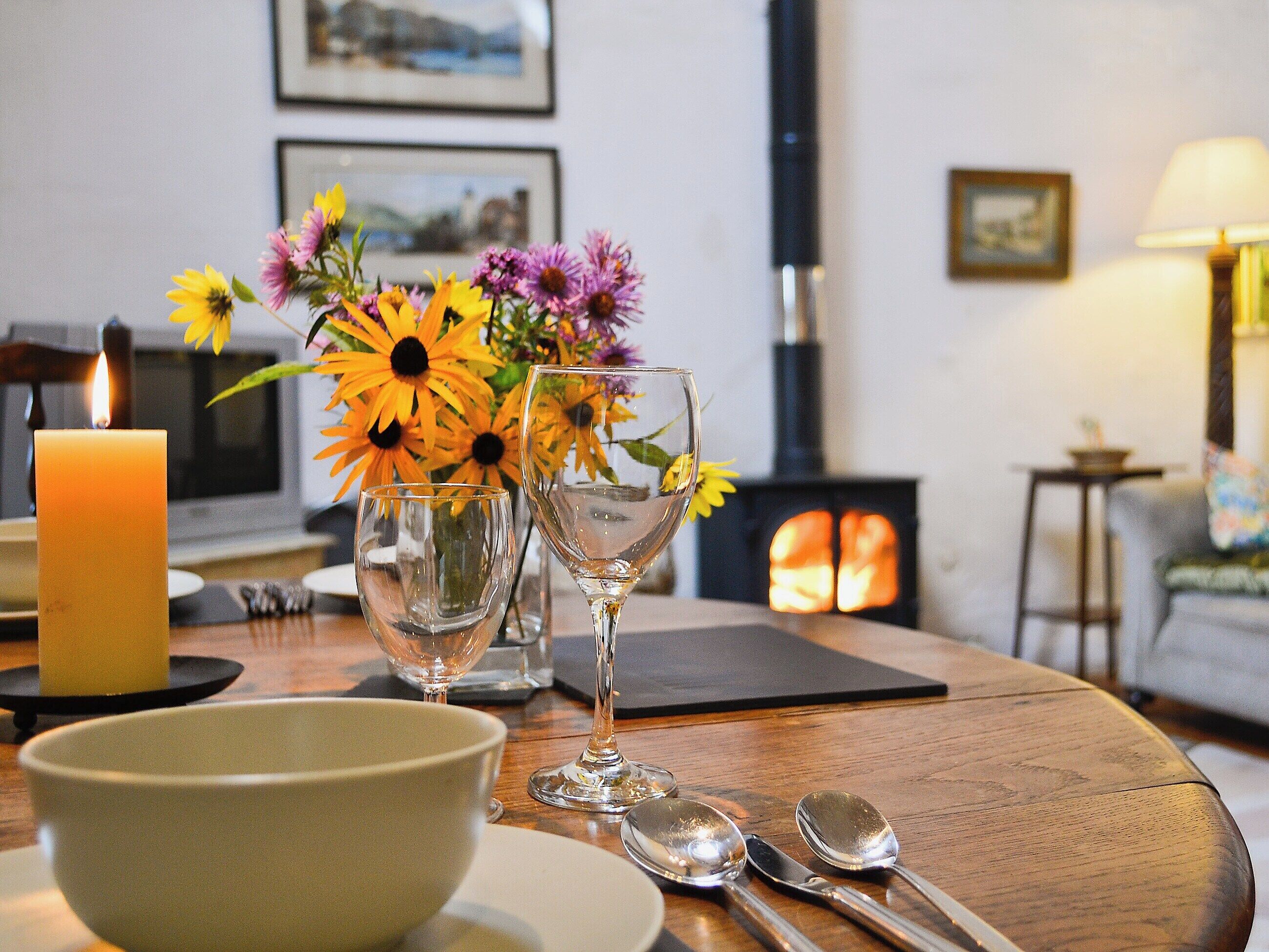Un coin repas chaleureux, agrémenté d’une bougie, d’un vase de fleurs et d’une cheminée en arrière-plan.